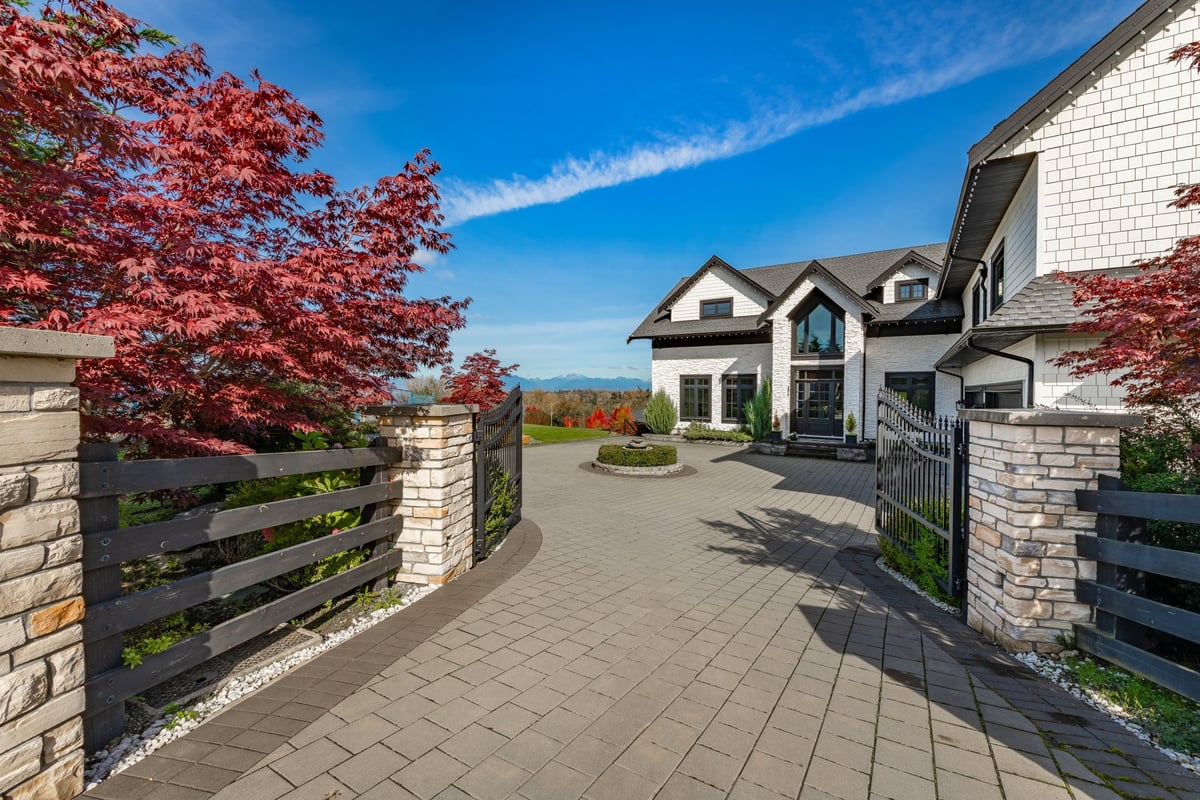 Elegant home with brick pillars, black wood trim, and landscaped driveway