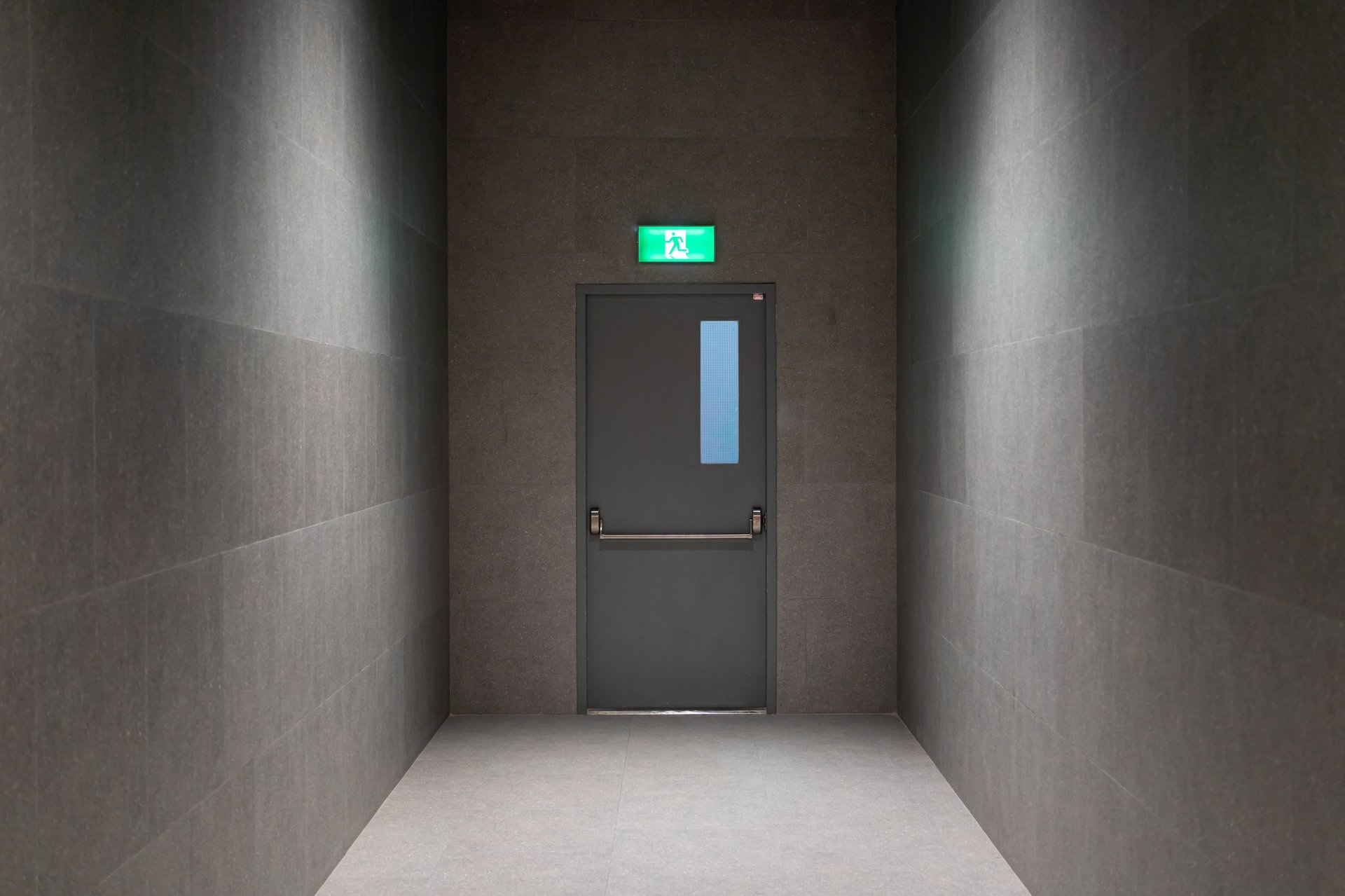 Modern Emergency Exit Door in Minimalist Dark Hallway with Overhead Light and Safety Sign