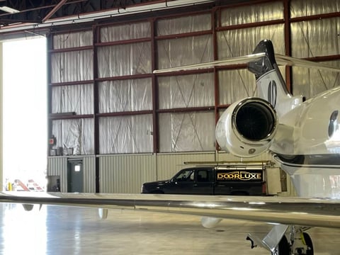 Private jet parked in hangar next to black luxury car with large window doors in background