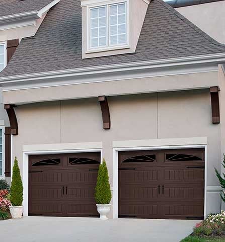 Two dark brown garage doors on a beige house with gray roof, white trim, and decorative brown brackets above