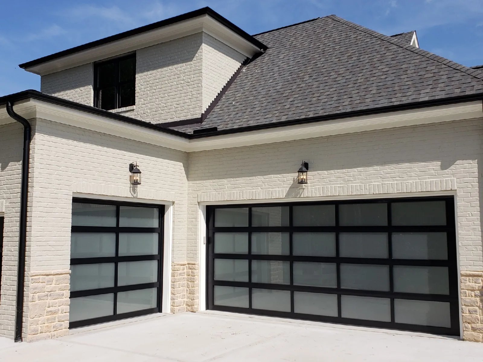 Modern white brick house with two dark framed garage doors and gray shingled roof