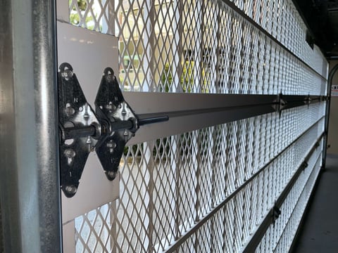Black decorative hinge on white mesh gate with horizontal metal bars