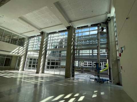 Empty industrial space with large glass doors and windows, concrete floor, and bright natural light casting shadows