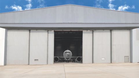 Large aircraft parked inside a metal hangar with open bay doors under blue sky