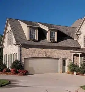 Two-story brick house with dormers, garage, and landscaping under clear blue sky