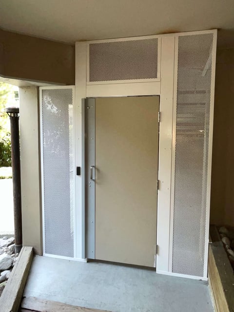 White metal door frame with mesh panels and closed metal door installed in room under construction