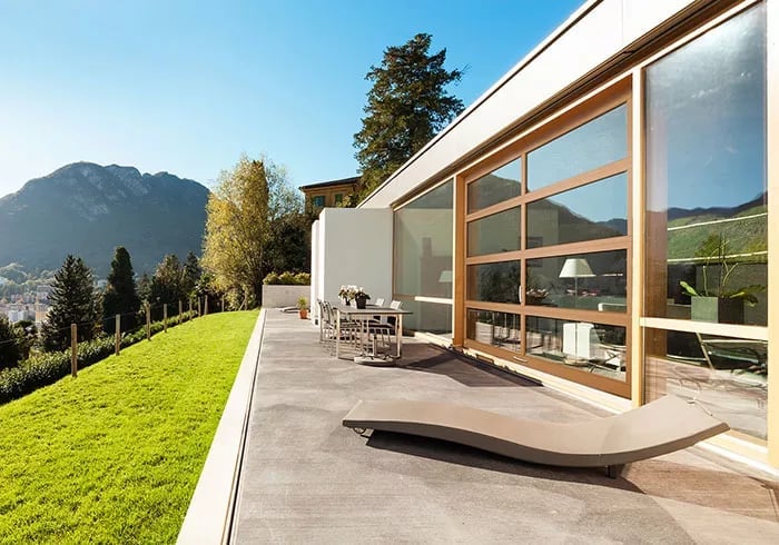 Modern house with large windows overlooking a green lawn and mountain landscape on a sunny day