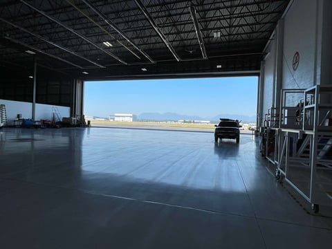 Empty aircraft hangar with a single black vehicle on a polished floor, mountains visible through open hangar doors