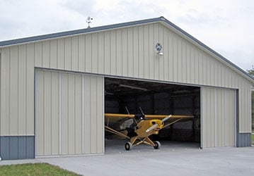 Yellow and black vintage aircraft parked in a metal hangar with open garage door