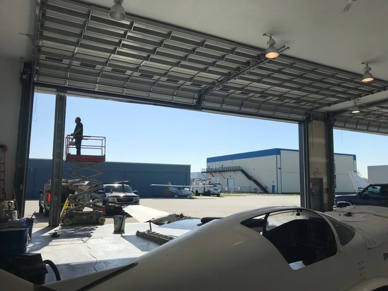 Commercial aircraft hangar with large industrial hangar doors open, showing planes and vehicles in BC facility