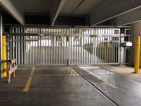 Closed metal security gate in underground parking garage with yellow bollards and concrete floor markings