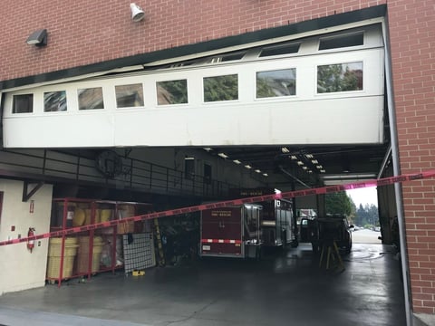 Fire truck parked inside an open garage bay with red caution tape across the entrance of a brick building