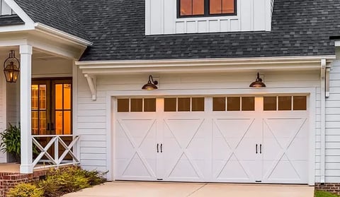 Modern white farmhouse with two-car garage door, brick chimney, and rustic front entrance with cross-pattern door and lanterns