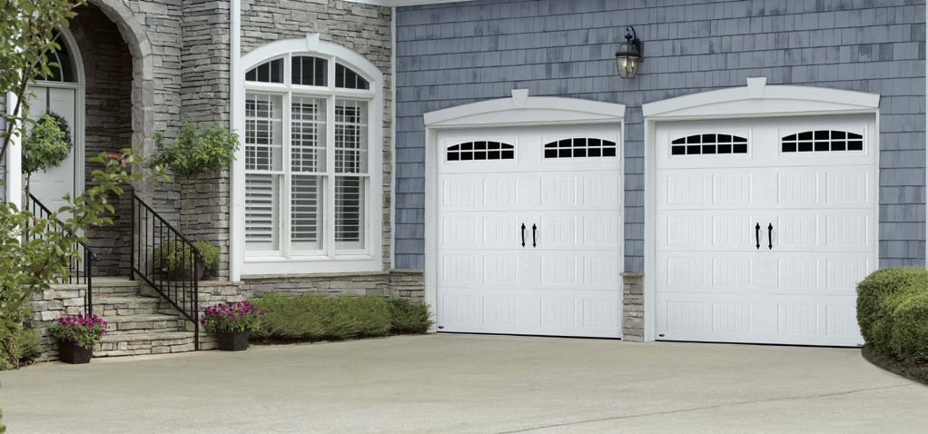 Modern house exterior with two white garage doors, arched entry door, and slate-blue siding