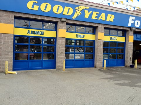 Goodyear tire shop storefront with blue roll-up doors labeled Alignment, Tuneup, and Brakes