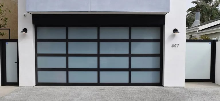Modern black aluminum garage door with frosted glass panels on white house facade