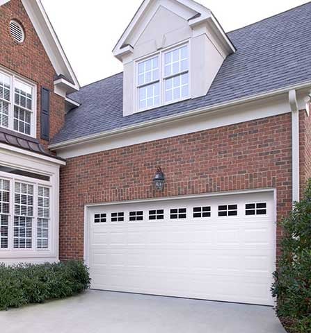 Two-car white garage door on red brick house with dormers and landscaping