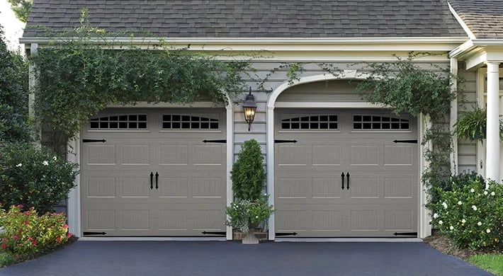 Two gray garage doors on a residential home with ivy-covered walls and landscaping