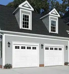 White two-car garage doors on a residential home with white trim, dormers, and dark roof