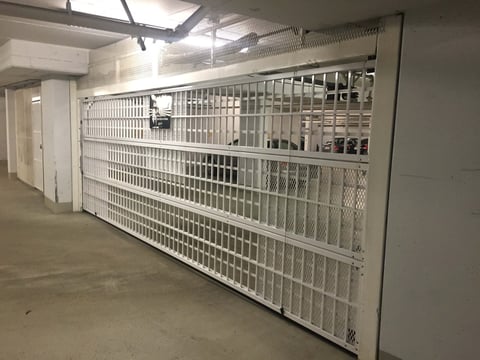 Row of white metal kennels or animal cages in an empty concrete facility with overhead lighting