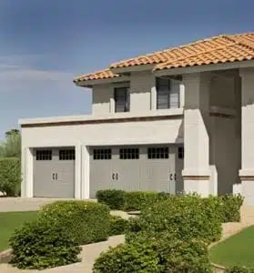 Modern two-story white house with clay tile roof, gray garage doors, and manicured landscaping in front