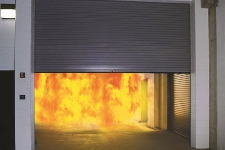 Intense fire and flames visible inside an industrial garage or warehouse with a partially open metal rolling door