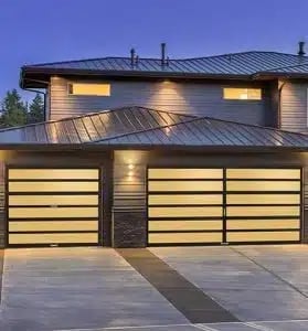 Modern two-story house with illuminated double garage doors, metal roof, and contemporary architectural design at dusk