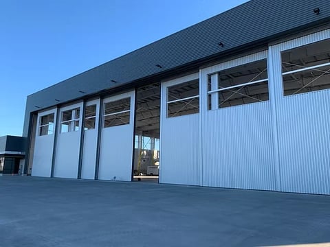 Modern industrial warehouse with large white metal garage doors and corrugated metal siding under clear blue sky
