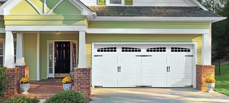 Yellow and green residential house with white garage doors, brick foundation, columns, and yellow planters on the driveway