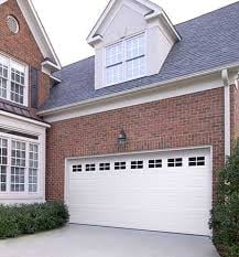Red brick residential home with white garage door, featuring gabled roof and landscaping