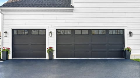 Two dark gray garage doors on a white house with plants on either side and gray driveway