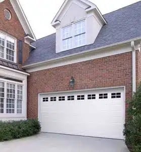 Modern brick house with white garage door, dormer window, and manicured landscaping