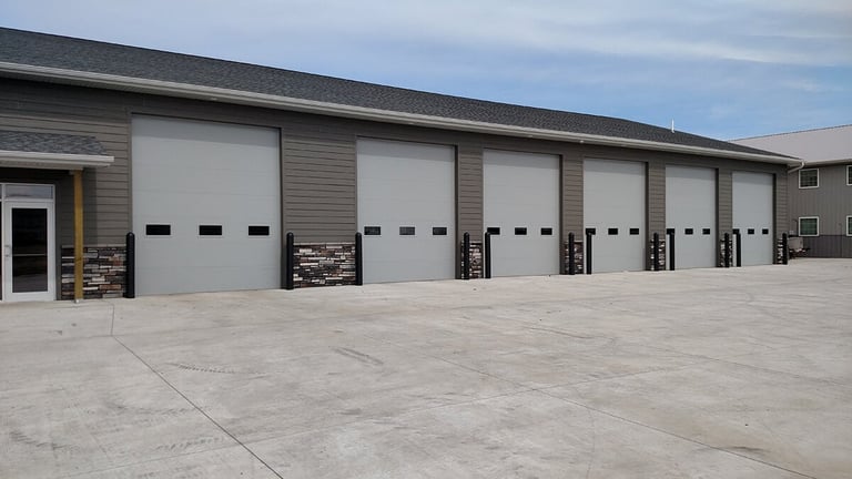 Industrial garage with five white overhead doors and concrete pad parking area