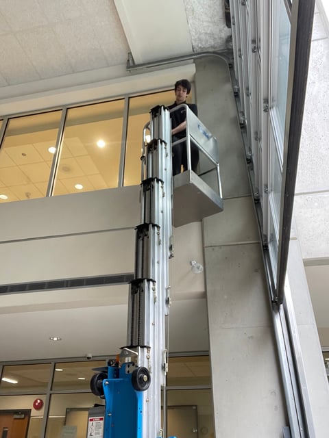 Worker on blue scissor lift elevated on building facade installing or inspecting exterior windows and cladding