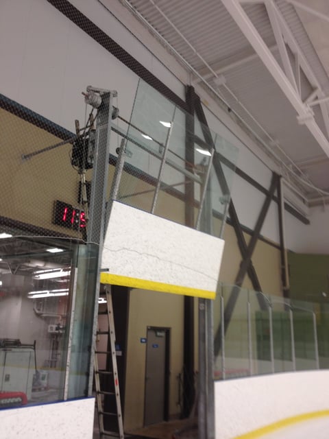 Industrial lift platform mounted on metal pole in warehouse or commercial facility with glass and metal framework overhead