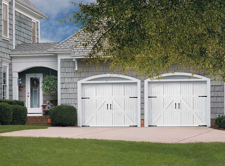 White two-car garage doors on shingled house with green landscaping and curved garage design