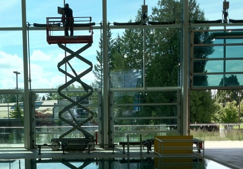 Worker on elevated scissor lift platform against industrial building frame with trees in background