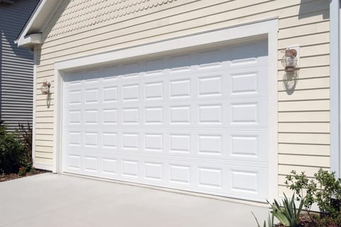 White residential garage door on beige house with concrete driveway and landscaping